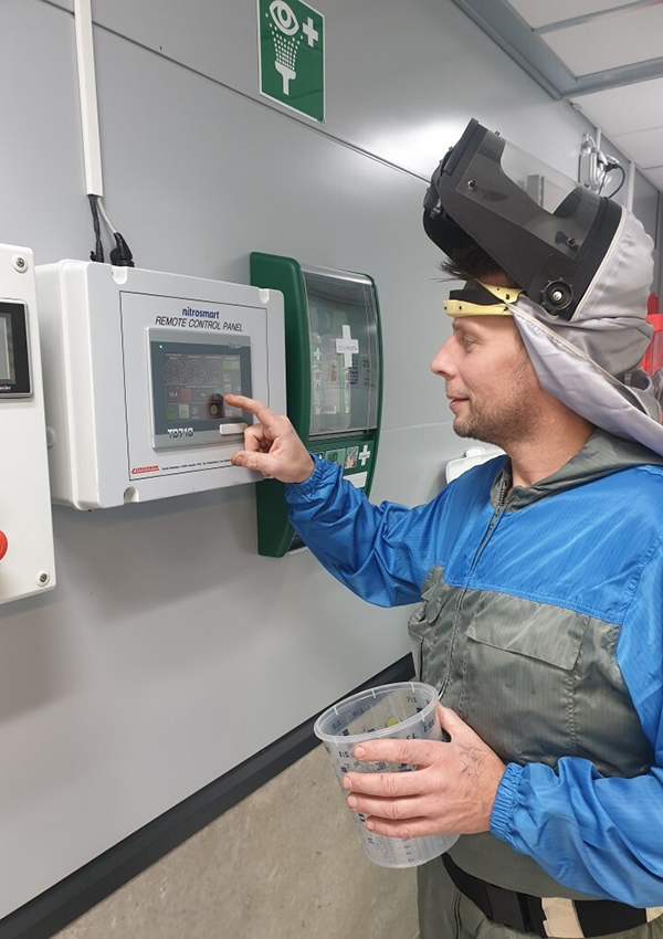 Person i svetshjälm och blå-grå overall framför Nitrosmart kontrollpanel. Personen klickar på skärmen med fingret.